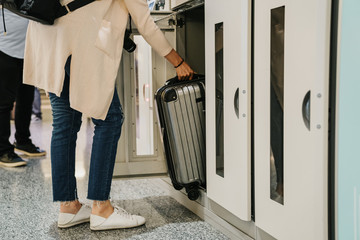 unrecognized asian woman in white shoes casual wear puts luggage to safety locker. Asian tourists use storage boxes for suitcase deposit. Backpacker takes stuff from coin container in airport.