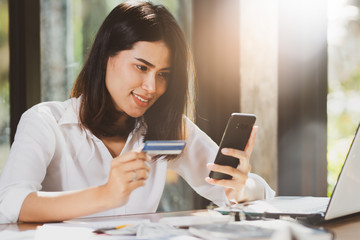 Asia woman looking at the credit card and using smartphone  smiles with happy.