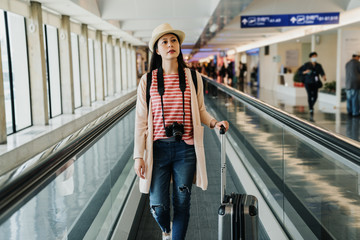 chinese girl traveler with camera walking on long horizontal escalator at international airport...