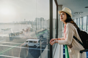Obraz premium modern international airport interior building view with female passenger relying on handrail curiously looking outside apron while boarding to airplane by using air gate bridge aviation architecture