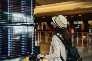 Back view of young traveler tourist woman in hat looking on schedule timetable waiting in lobby hall at international airport. female passenger travel abroad on weekends getaway. Air flight concept