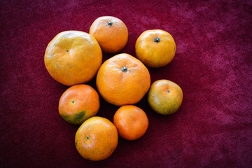 Pile of orange fruit various sizes on red dark background