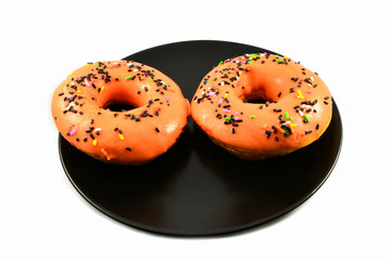 Orange donuts with sprinkles on black plate on white background