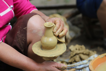 Closeup of earthenware molding on pottery wheel by skillful elderly Asian woman's hand. Thailand. 