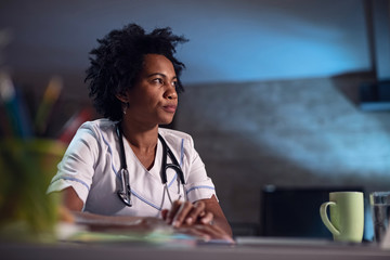 Serious African American nurse sitting at desk in doctor's office.