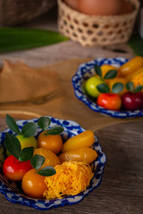 Thai desserts on a plate of white and blue stripes placed on wood table there are Similar object, fork, pandan, coconut, egg in basket and golden cloth placed on the back side.