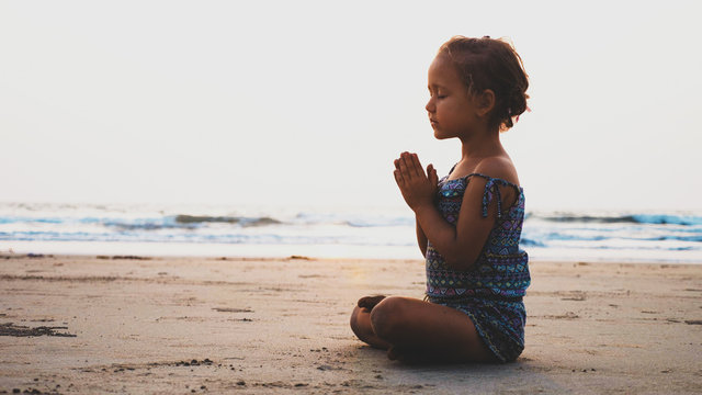 Vintage image of cute little girl sits in lotus pose and meditating on sandy beach