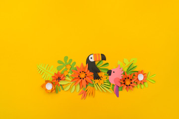 Decorative composition of tropical leaves and flowers. Yellow background. Toucan bird and pink parrot. Paper craft.