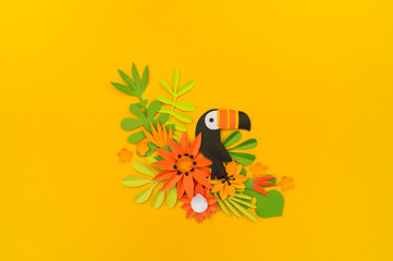 Decorative composition of tropical leaves and flowers. Paper craft. Yellow background. Toucan bird.
