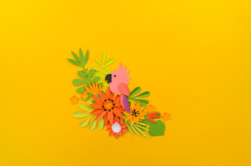 Decorative composition of tropical leaves and flowers. Paper craft. Yellow background. Pink parrot.