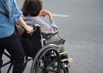 Closeup of elderly disabled  Asian woman  in wheelchair assists by female assistant. Symbol of ageing society. 