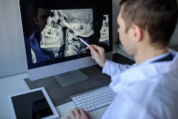 back view of a male radiologist examining neck x-rays (cervical vertebrae) on computer
