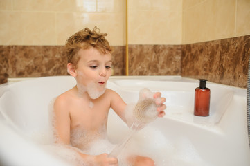 Little boy washing and playing in bathtub with foam and soap bubbles