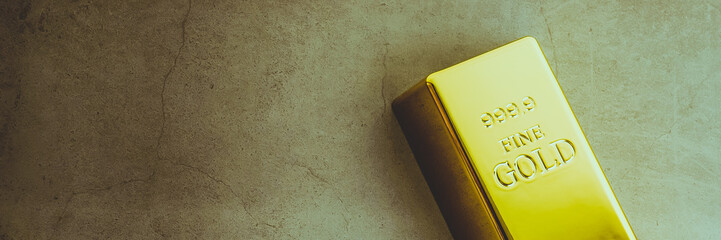 An ingot of gold metal bullion of pure brilliant diagonally located on a gray textured background.
