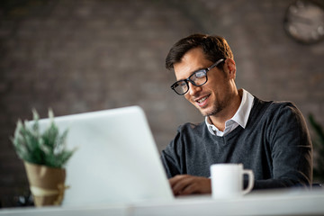Smiling businessman working on laptop while sitting at desk in the office.