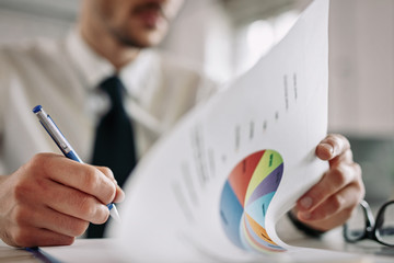 Close up of businessman taking notes while analyzing charts at work.