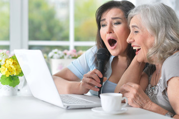 Two mature women singing karaoke with laptop