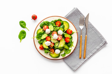 Fresh salad with mozzarella, spinach, cherry tomatoes, cucumber on plate on white background top...