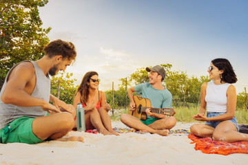 Lifestyle beach of group of young friends playing guitar and enjoying