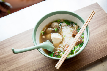 Rice vermicelli noodle and meatball Braised pork and tofu pork in the bowl have chopstick and spoon on the wood table