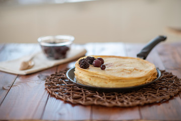 A stack of homemade pancakes on a frying pan, brown background