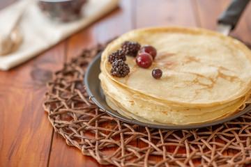 A stack of homemade pancakes on a frying pan, brown background