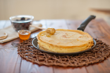 A stack of homemade pancakes on a frying pan, brown background