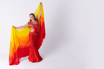 Fototapeta premium Young girl with shawl and in red dress performs oriental dance on white background