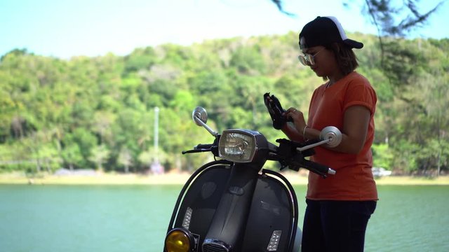 Young woman parking a scooter beside the lake.