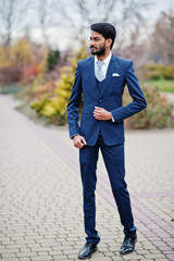 Stylish beard indian man with bindi on forehead, wear on blue suit posed outdoor.