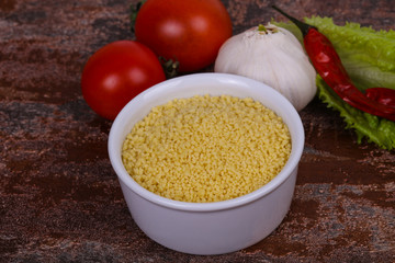 Raw couscous in the bowl served salad leaves, tomato and pepper