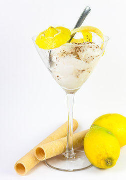 HELADO DE LIMÓN EN COPA CON CÁSCARA CORTADA, BARQUILLOS DE GALLETA Y LIMONES SOBRE FONDO BLANCO