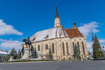 Fototapeta na wymiar St. Michael's Church and Matthias Corvinus Monument in the city center of Cluj-Napoca, Romania during a sunny day with blue sky