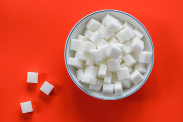 White bowl filled with sugar cubes isolated on a red background