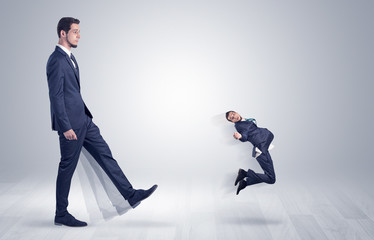 Big man in suit kicking out little himself with simple white wallpaper
