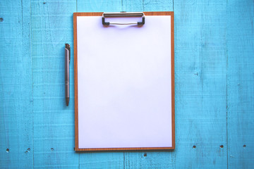 Clipboard with white sheet on wood background. Top view.Vintage style.