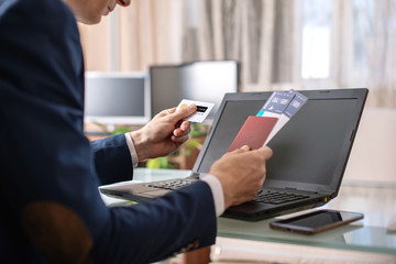 Man holding airline ticket and debit card buying on the Internet using a laptop. Purchasing and booking online