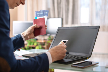 Man holding airline ticket and debit card buying on the Internet using a laptop. Purchasing and booking online