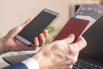 Man holding airline ticket and phone in hand buying on the Internet using a laptop. Purchasing and booking online