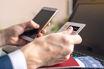 Man holding debit card and phone in hand buying on the Internet airline tickets. Purchasing and booking online