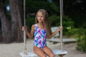 Cute girl with long hair in a swimsuit on a swing on the beach. vacation concept.