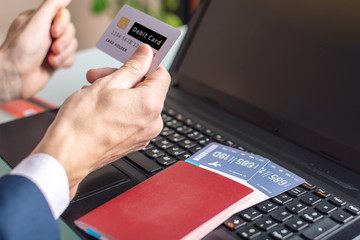 Man holding debit card in hand buying on the Internet airline tickets using a laptop. Purchasing and booking online