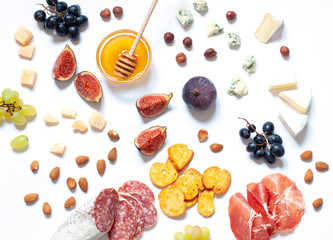 Antipasti food white flat lay with nuts, honey, cured meat, salami, cheeses, grapes and figs. Top...