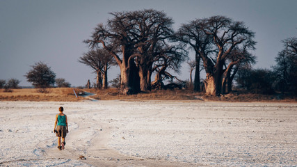 Fototapeta na wymiar Frau läuft über die Salzpfanne in Richtung Baines Baobabs, Nxai Pans National Park, Botswana