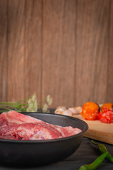 Fresh pork in a black pan, placed on a wooden table with spices placed around.