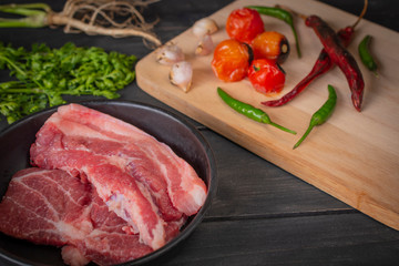 Fresh pork in a black pan, placed on a wooden table with spices placed around.