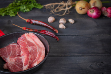 Fresh pork in a black pan, placed on a wooden table with spices placed around.