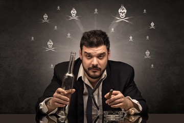 Loser drunk man sitting at table with skulls concept around
