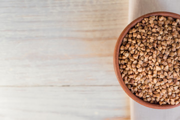 Dry buckwheat in brown clay bowl on wooden table. gluten free grain for healthy diet