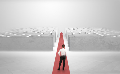 Businessman going straight ahead on a red carpet arrow between two maze
